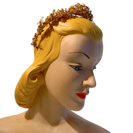 A vintage-style gold tiara with leaf-like detailing, shown on a blonde mannequin head against a plain white background.